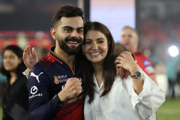 Virat Kohli holding the IPL 2025 trophy with wife Anushka Sharma standing beside him, both smiling and celebrating the victory.